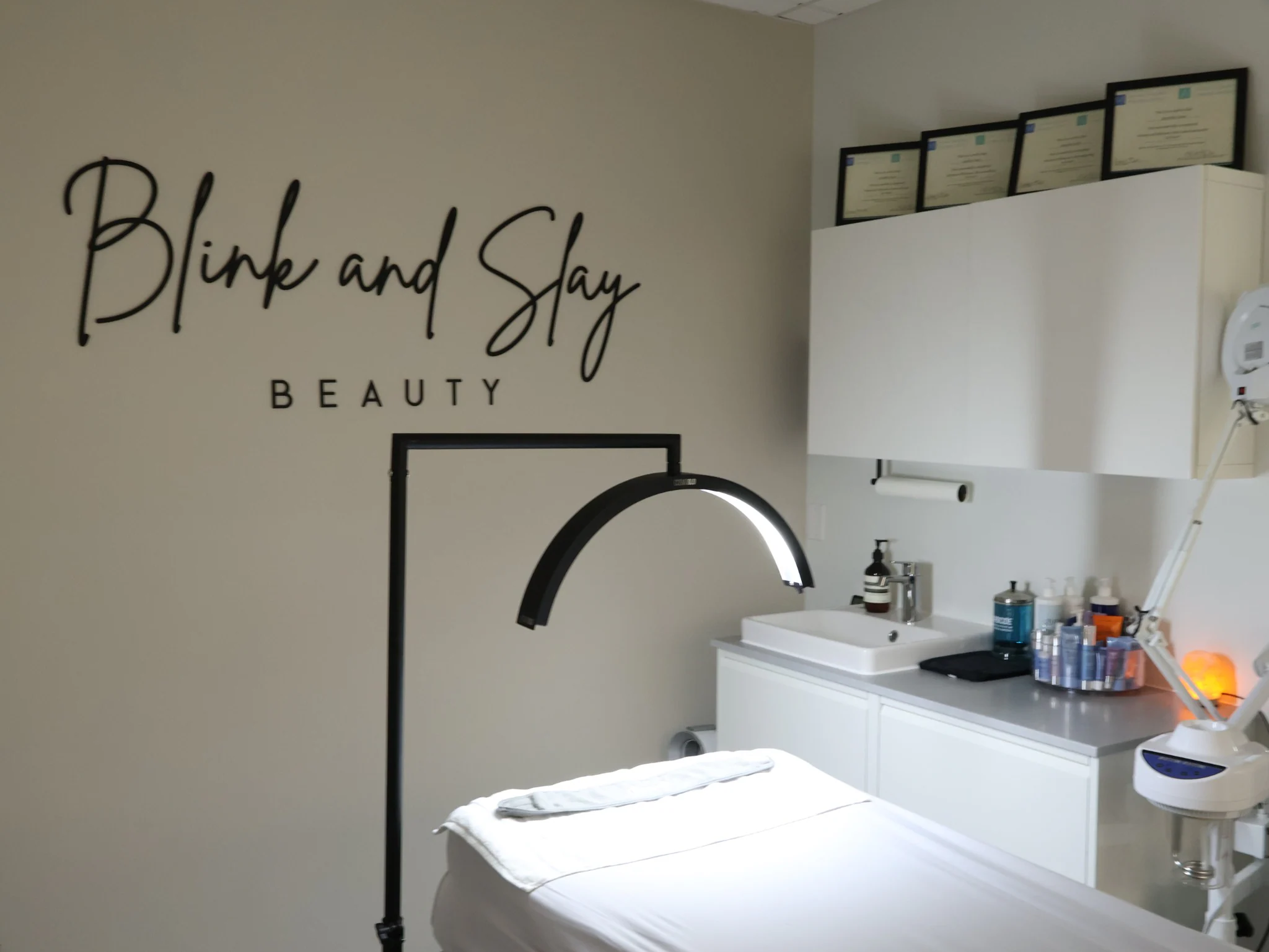 Blink & Slay Beauty treatment room with a treatment bed, wall sign, and skincare station.